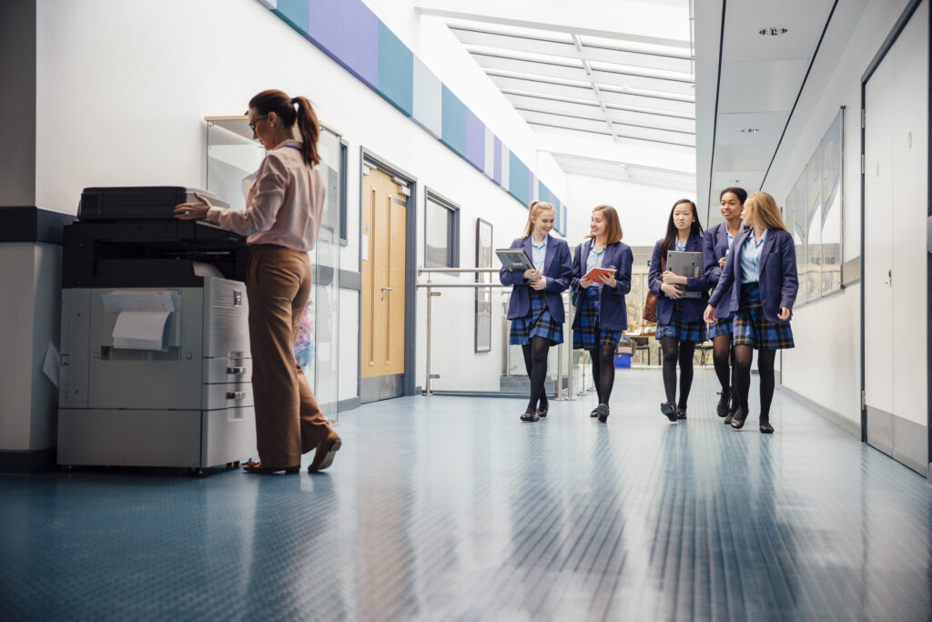 school girls in school hallway with adult woman using hp printer photocopier