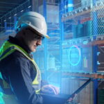 yellow vest warehouse worker using laptop to digitally manage inventory